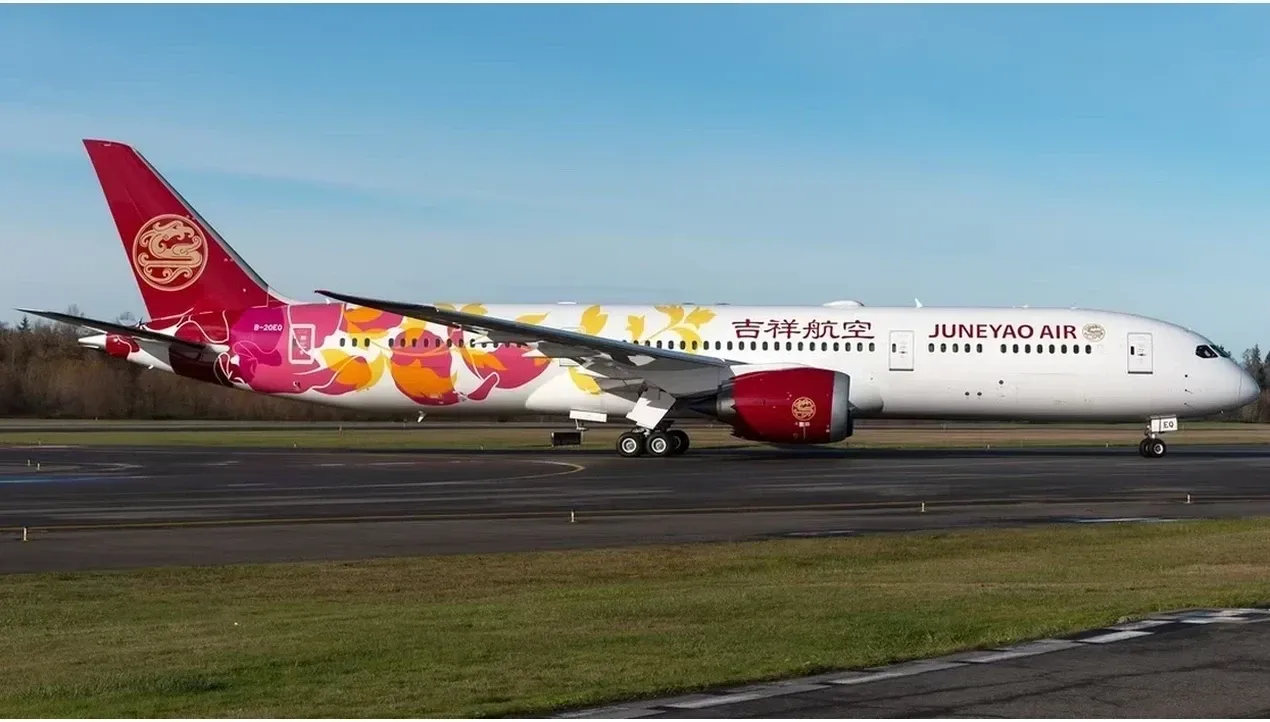 A Juneyao Airlines Boeing 777 sits on the tarmac with vibrant red and gold livery details highlighting the aircrafts exterior