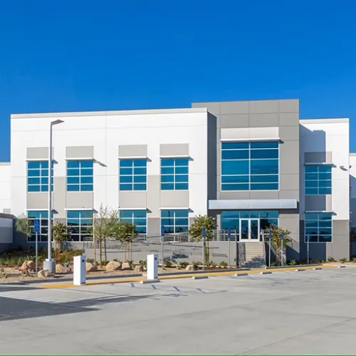 A modern gray commercial building with large windows dominates the scene alongside a paved parking lot and landscaping