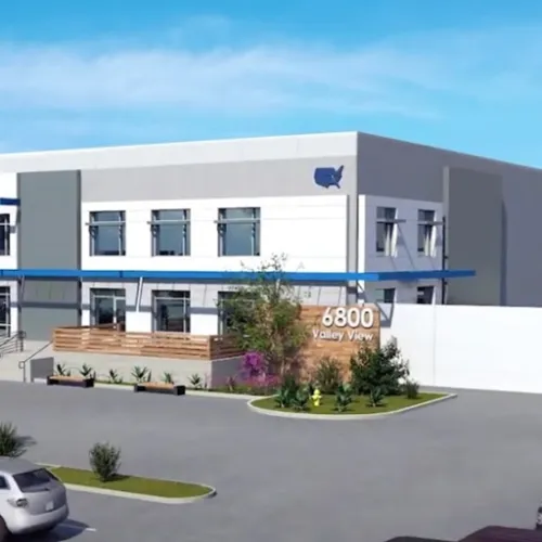 A modern commercial building with a lightcolored exterior and landscaping sits on a street The scene includes a sidewalk and