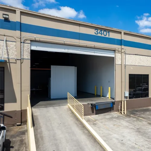 A large industrial building with a blue and white striped door is visible here The concrete ground is wet and a ramp leads