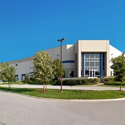 A modern building with large blue windows and a gray facade sits on an asphalt road surrounded by green grass A street lamp