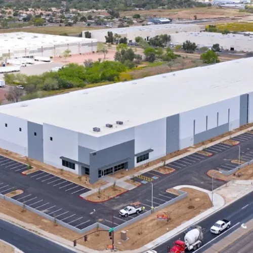 A large industrial warehouse with a white roof dominates the scene a lightcolored parking lot extends across the foreground