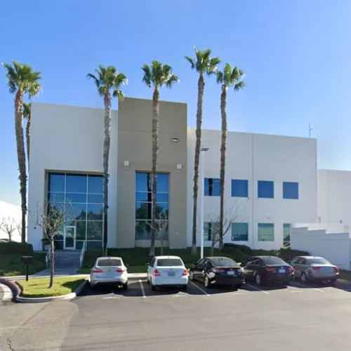 A modern building with large windows stands prominently against a grassy slope shaded by palm trees Several parked cars are