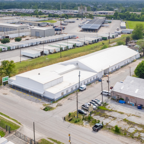A large industrial building with a white roof dominates the scene presenting a commercial storage facility with multiple