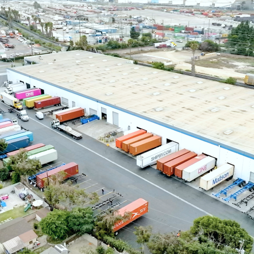 Orange shipping containers line a long concrete pier at the Port of Long Beach Several trucks are visible in the background
