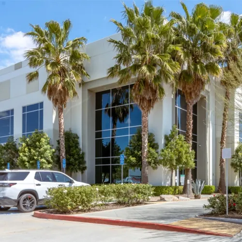 A modern building with large glass windows stands in front of a red striped parking area A white SUV is parked nearby and